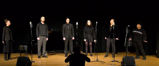 Singers on stage dressed in black for collegiate concert.